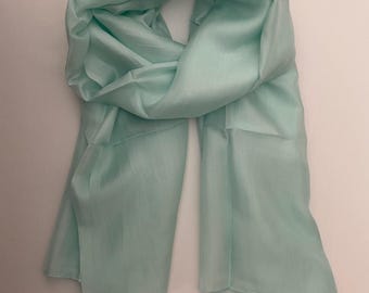 Puede incluir: Una bufanda verde claro hecha de una tela suave y fluida. La bufanda está drapeada y doblada, mostrando su textura y color. La bufanda parece estar hecha de seda o un material similar, perfecta para añadir un toque de elegancia a cualquier atuendo.
