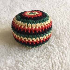 Puede incluir: Una bola de crochet con rayas rojas, amarillas, verdes y negras.