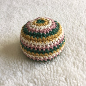 Puede incluir: Una bola de crochet con rayas de hilo rosa, blanco, verde y amarillo.