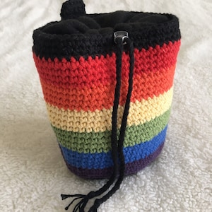 May include: A rainbow crocheted drawstring bag with a black fleece lining. The bag has a black drawstring and is made with a variety of colourful yarns.