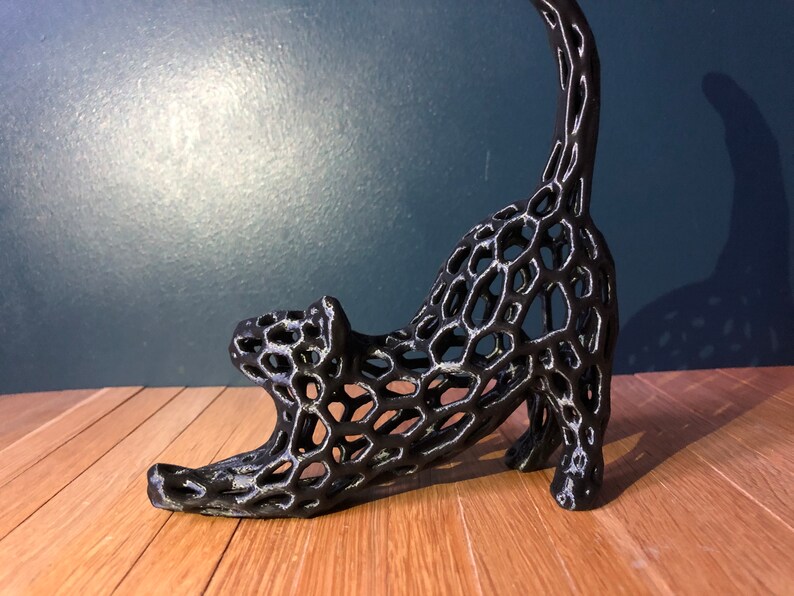 Op de afbeelding: Zwarte, 3D-geprinte kattenfiguur met een traliewerkontwerp. De kat staat in een rekhouding met zijn staart omhoog.