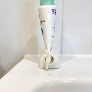 May include: White plastic tube squeezer with a blue and white tube of hand cream inserted. The tube is labeled "Refreshing Body Lotion".