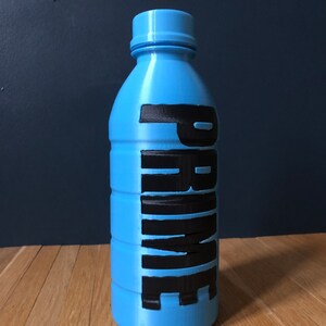 Op de afbeelding: Een blauwe plastic fles met het woord "PRIME" in zwarte letters.