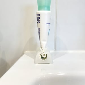 May include: White plastic tube holder with a white tube of lotion inside. The holder has a hole in the bottom to dispense the lotion.