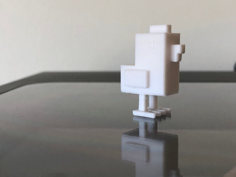 Op de afbeelding: Een wit 3D-geprint model van een gestileerde kip. De kip heeft een blokvormig ontwerp met een kleine snavel en poten.