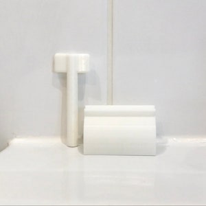 May include: White plastic toilet tank lever and handle. The lever is rectangular and has a small handle on the top. The handle is round and has a small hole in the center.