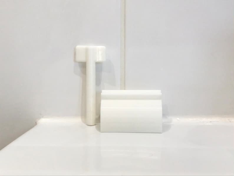 May include: White plastic toilet tank lever and handle. The lever is rectangular and has a small handle on the top. The handle is round and has a small hole in the center.