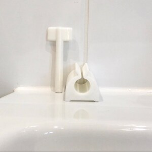 May include: White plastic bathroom accessories, including a small, vertical, T-shaped handle and a round, open-ended, ring-shaped holder.