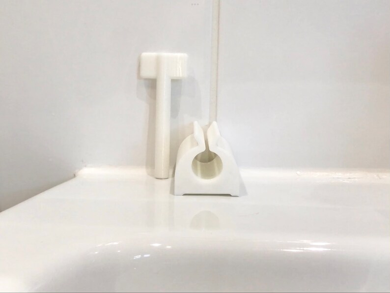 May include: White plastic bathroom accessories, including a small, vertical, T-shaped handle and a round, open-ended, ring-shaped holder.