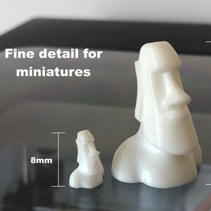 Op de afbeelding: Twee witte 3D-geprinte miniatuurbeeldjes van Paaseilandhoofden. Het grotere beeldje is 20 mm hoog en het kleinere beeldje is 8 mm hoog.  Fijne details voor miniaturen.