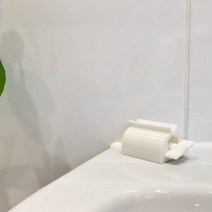 May include: White plastic toothbrush holder mounted on a white tiled bathroom wall.
