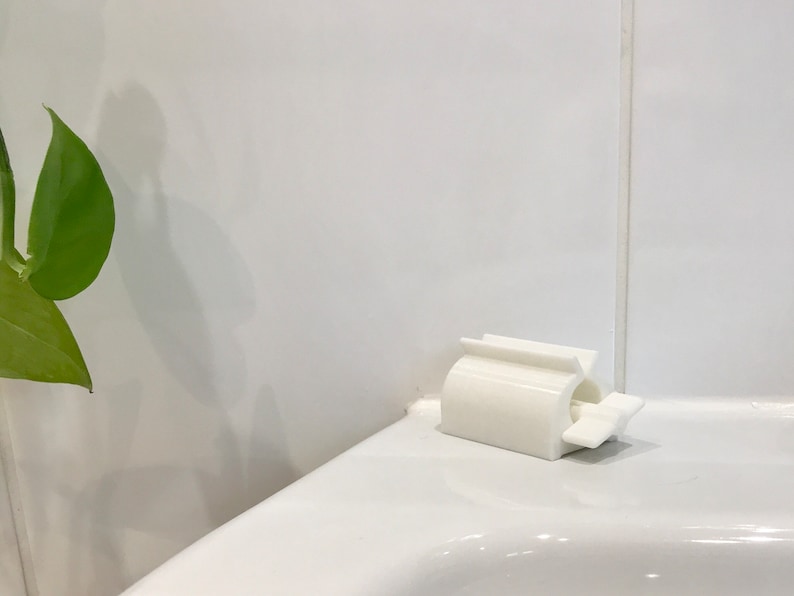 May include: White plastic toothbrush holder mounted on a white tiled bathroom wall.