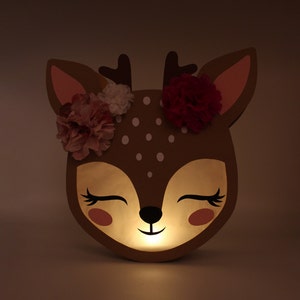 May include: A brown deer-shaped nightlight with a white polka dot pattern and pink and red flowers on its head. The light is on and glowing.