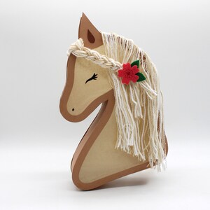 May include: A brown wooden horse head with a white yarn mane and a red flower with green leaves.