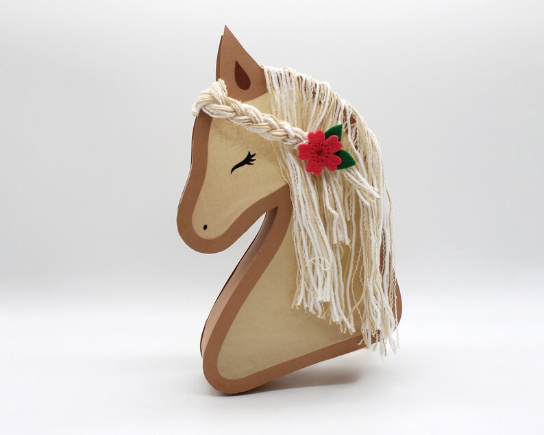 May include: A brown wooden horse head with a white yarn mane and a red flower with green leaves.