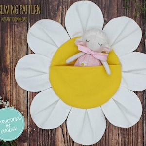 Puede incluir: Una flor de margarita de fieltro blanco con un centro amarillo. Una pequeña muñeca de cordero blanco con un vestido rosa está acostada en el centro de la flor. El texto "PDF SEWING PATTERN" y "INSTANT DOWNLOAD" está en la parte superior de la imagen. El texto "INSTRUCTIONS IN ENGLISH!" está en un círculo en la parte inferior izquierda de la imagen.