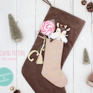 Op de afbeelding: Een bruine kerstsok gevuld met een roze bloemenpatroon kous, een hertje knuffel en een spiraallolly. Een gouden letter "C" bedel en een kwastje hangen aan de kous. De tekst "PDF Sewing Pattern" en "Instructions in English" zijn zichtbaar.