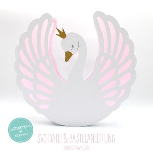 Op de afbeelding: Een witte papieren zwaan met roze vleugels en een gouden kroon. De zwaan staat op een witte achtergrond. De tekst "SVG Datei & Bastel Anleitung" staat onder de zwaan.