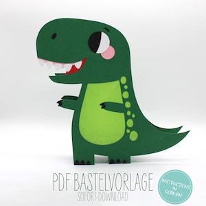 Op de afbeelding: Groene papieren dinosaurus met een grote glimlach en grote ogen. De dinosaurus heeft een gestippeld patroon op zijn rug en staart. De tekst "PDF Baste Vorlage" en "Sofort-Download" staat onderaan de afbeelding. Instructies in het Duits staan in een cirkel rechtsonder.