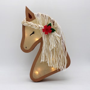May include: A wooden horse head cutout with a light inside. The horse has a white yarn mane and a red felt flower with green leaves.