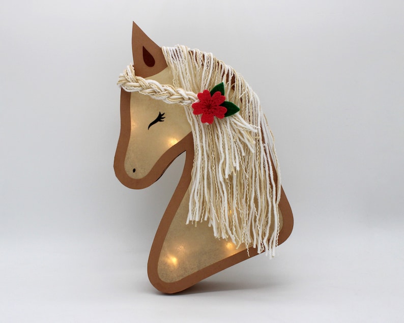 May include: A wooden horse head cutout with a light inside. The horse has a white yarn mane and a red felt flower with green leaves.