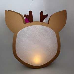 May include: A brown cardboard reindeer-shaped lantern with a white paper insert and a small light inside. The reindeer has brown antlers and a white pom-pom on each antler.