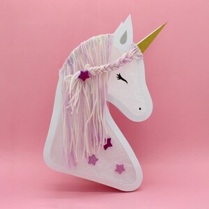 May include: White paper unicorn head with a pink and white yarn mane and horn. The unicorn has pink glitter stars on its face.