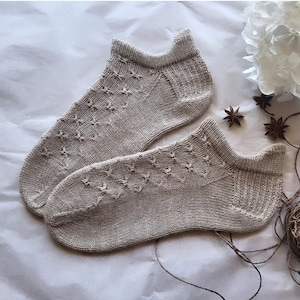 May include: A pair of beige knitted ankle socks with a star pattern. The socks are made of a soft, comfortable material and are perfect for everyday wear.