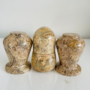May include: Three decorative containers made of brown and beige marbled stone. The containers are round and have a smooth, polished finish.