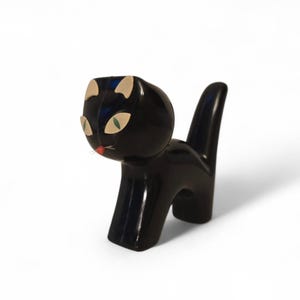 May include: A black cat ornament with a glossy finish. The cat has tan ears, green eyes, and a red nose. The figurine is in a standing pose with its tail upright.