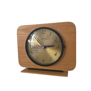 Puede incluir: Un reloj vintage de madera con una esfera dorada y agujas negras. La esfera del reloj dice "PRIM ELECTRONIC".