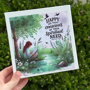 May include: Square canvas art print featuring a serene illustration of a person reading by a stream. The artwork includes the text "Happy are those conscious of their spiritual need" from Matthew 5:3. The print has a white border and a green and white scalloped edge.