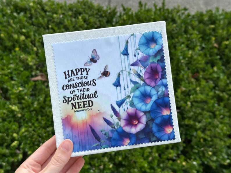 May include: A square canvas print featuring a watercolor design of blue and purple morning glory flowers, butterflies, and the text "HAPPY are those conscious of their Spiritual NEED Matthew 5:3". The print is held by a hand.