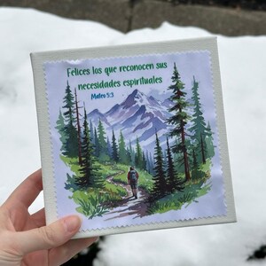 Puede incluir: Un lienzo cuadrado blanco roto con una imagen impresa de una escena de monta&ntilde;a y texto en espa&ntilde;ol. La imagen muestra a una persona caminando por un sendero a trav&eacute;s de un bosque, con monta&ntilde;as al fondo. El texto dice "Felices los que reconocen sus necesidades espirituales Mateo 5:3."