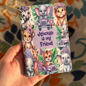 May include: A colorful wallet featuring cartoon animals, including a zebra, elephant, lion, and tiger, surrounded by flowers and greenery. The text "Jehovah is my Friend" is displayed in the center. The wallet has a soft, leather-like texture.