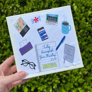 May include: A white canvas with various illustrated elements, including a textbook, candy, a phone, a coffee mug with "Pioneer Fuel", a notepad with the text "Fully Accomplish Your Ministry", glasses, and a book titled "Holy Scriptures".
