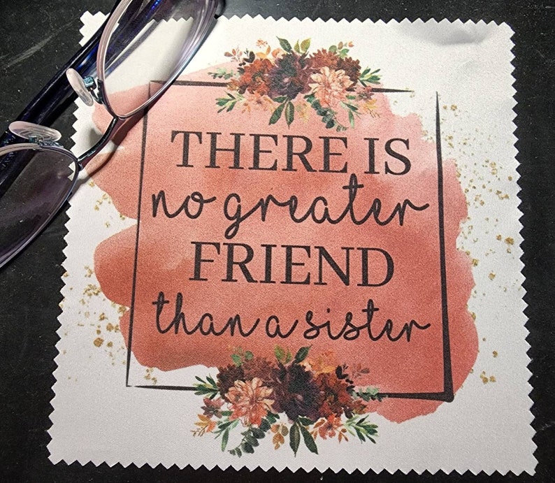 Puede incluir: Un pa&ntilde;o de limpieza de microfibra cuadrado blanco con un fondo de acuarela rosa y purpurina dorada. El pa&ntilde;o tiene un borde negro y el texto "THERE IS no greater FRIEND than a sister" en negro.