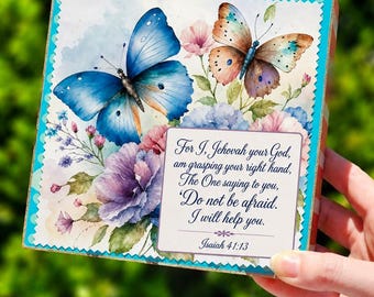 May include: A square decorative sign featuring a watercolor illustration of a large blue butterfly and a smaller orange butterfly surrounded by purple and pink flowers. A white rectangular inset displays the text: For I, Jehovah your God, am grasping your right hand, The One saying to you, 'Do not be afraid. I will help you.' Isaiah 41:13.