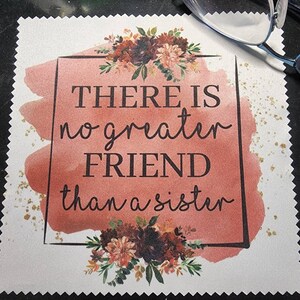Puede incluir: Un cuadrado de tela blanca con un fondo de acuarela rosa y purpurina dorada. El texto "THERE IS no greater FRIEND than a sister" est&aacute; escrito en un marco negro con un dise&ntilde;o floral.