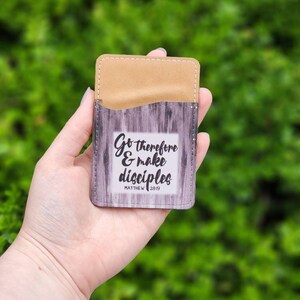 May include: A brown leather card holder with a wood grain design and the text "Go therefore & make disciples Matthew 28:19"
