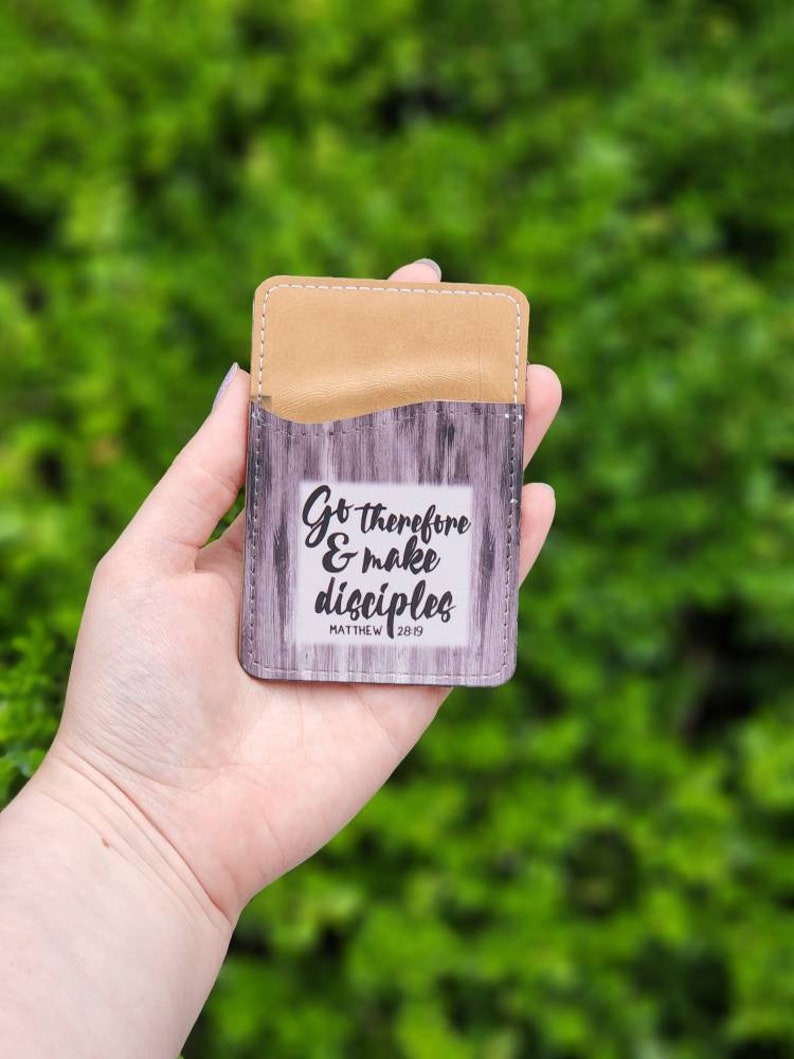 May include: A brown leather card holder with a wood grain design and the text "Go therefore & make disciples Matthew 28:19"