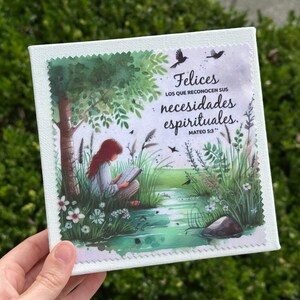 May include: Square canvas art print featuring a serene illustration of a person reading under a tree near a stream. The artwork includes text in Spanish: "Felices los que reconocen sus necesidades espirituales. Mateo 5:3."