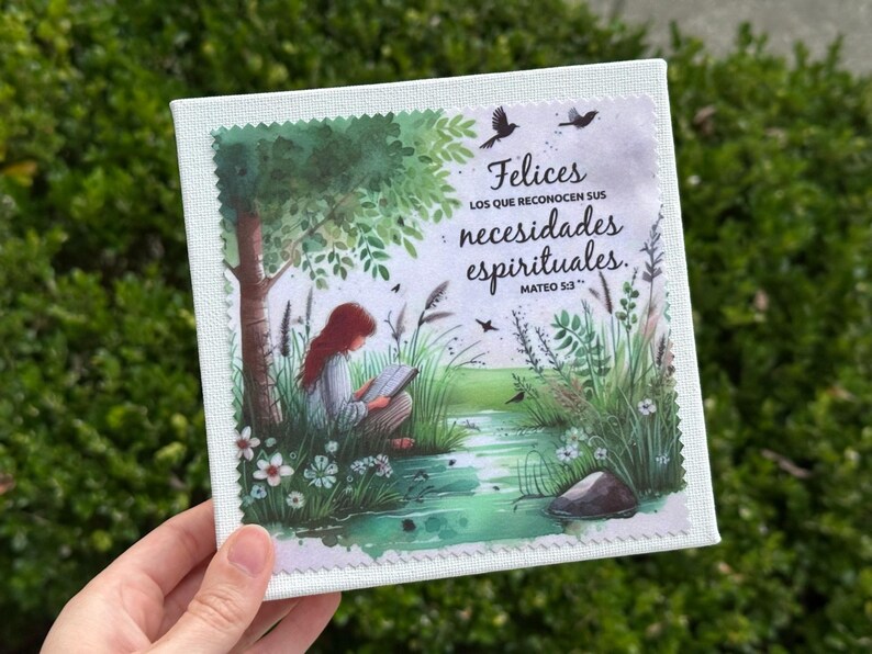 May include: Square canvas art print featuring a serene illustration of a person reading under a tree near a stream. The artwork includes text in Spanish: "Felices los que reconocen sus necesidades espirituales. Mateo 5:3."