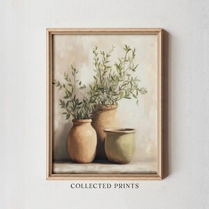 May include: A framed art print featuring three ceramic vases in varying sizes and colors, each holding green leafy branches. The vases are in shades of tan and olive green, set against a neutral background. The text "COLLECTED PRINTS" is at the bottom.
