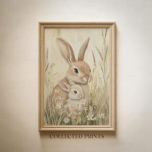 Puede incluir: Una impresión enmarcada que presenta una madre coneja y un bebé conejo acurrucados en un campo de hierba alta y flores silvestres. La obra de arte está realizada en tonos suaves y apagados de beige, marrón y crema. El texto "COLLECTED PRINTS" está en la parte inferior.