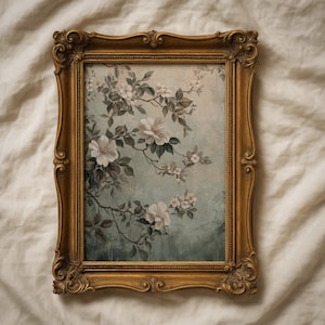 May include: A framed floral print featuring white flowers and green leaves against a soft blue-green background. The artwork is enclosed in an ornate, gold-colored frame, adding a vintage aesthetic. The overall theme is botanical and decorative.