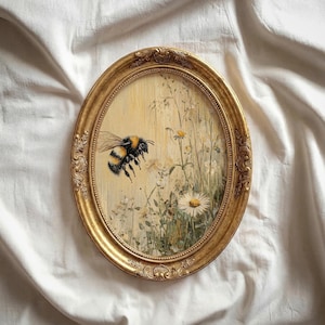 May include: A vintage-style, oval painting in a gold frame, depicting a bumblebee flying near daisies and wildflowers. The artwork has a light yellow background and detailed brushstrokes, evoking a classic aesthetic.