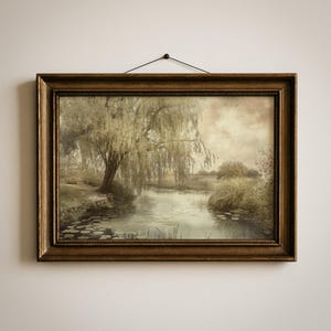 May include: A framed landscape painting depicts a serene pond scene with a weeping willow tree. The artwork features muted tones of green, brown, and beige, with a golden-brown frame. The painting is hung on a white wall.