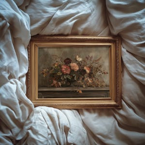 May include: A framed floral still life painting featuring a bouquet of roses in shades of red, peach, and cream. The painting is set in a gold ornate frame. The artwork is displayed on a white, textured surface.