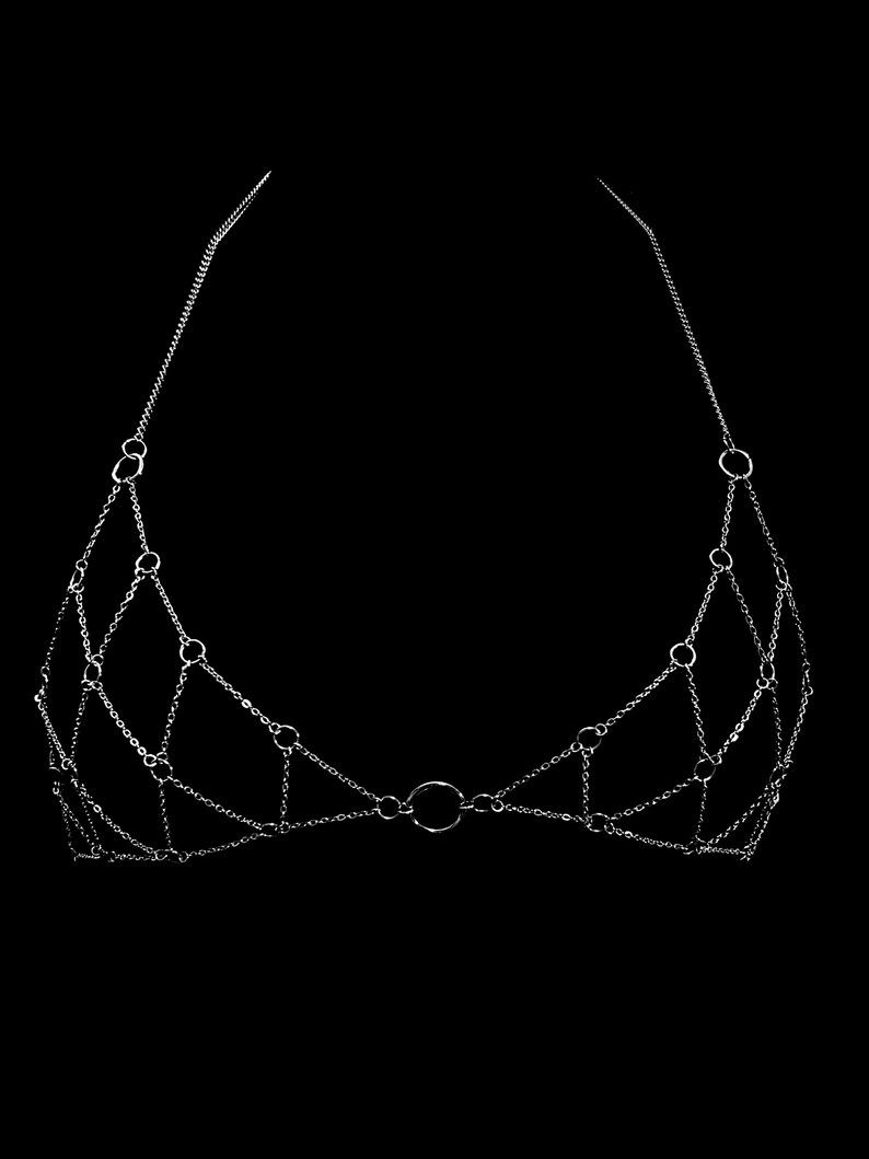 May include: A silver chain body jewelry piece with a circular design. The chain is made of small, interconnected links.